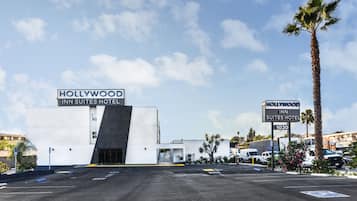 A modern building with a sign reading "Hollywood Inn Suites Hotel" and a parking lot in front.