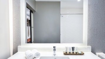 A bathroom with a large mirror, a sink, and toiletries.
