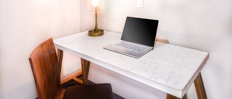 A small, modern workspace with a laptop on a marble table, a wooden chair, and a floor lamp.