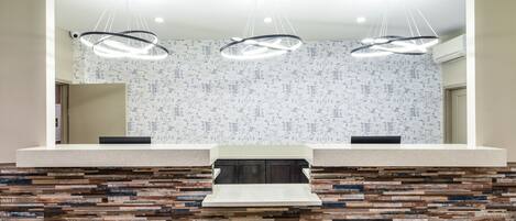 A modern reception area with a stone mosaic backsplash, three pendant lights, and a central counter.