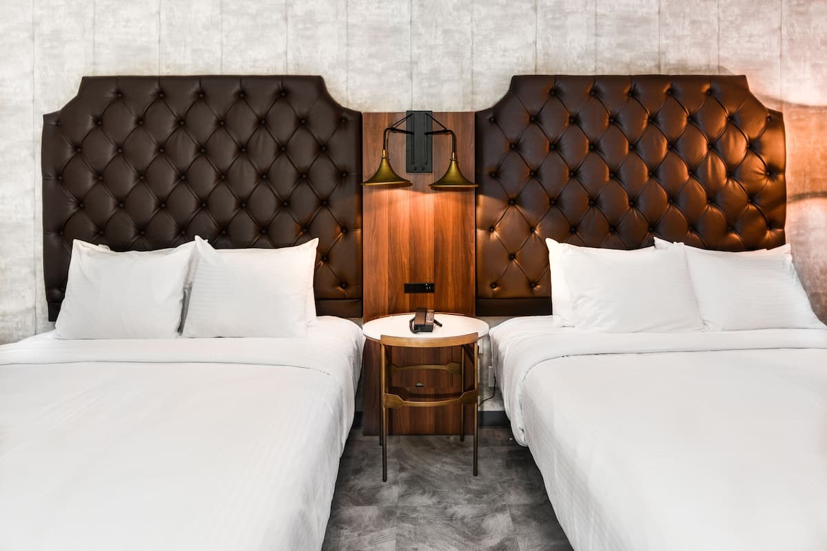 A hotel room with two beds, a wooden nightstand, and a wall-mounted lamp.