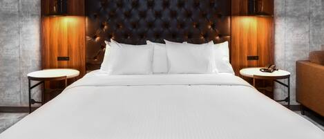 Uma cama grande com cabeceira estofada, duas mesas de cabeceira e um criado-mudo de madeira.
