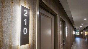 Un pasillo de hotel con puertas numeradas 210 y 211, que presenta un diseño moderno con un revestimiento texturizado e iluminación empotrada.