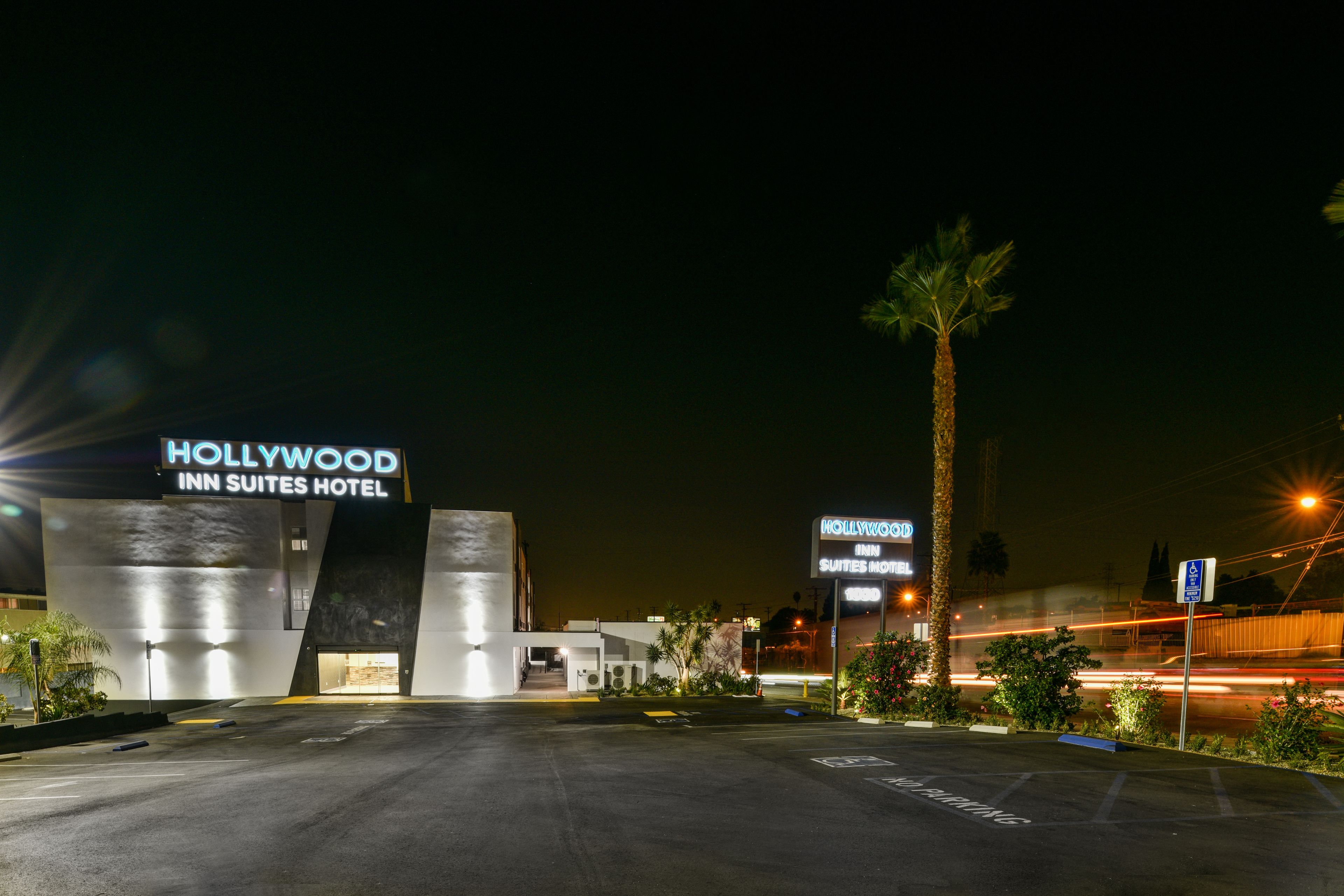 The Hollywood Inn Suites Hotel entrance with a modern design, palm trees, and a parking lot.