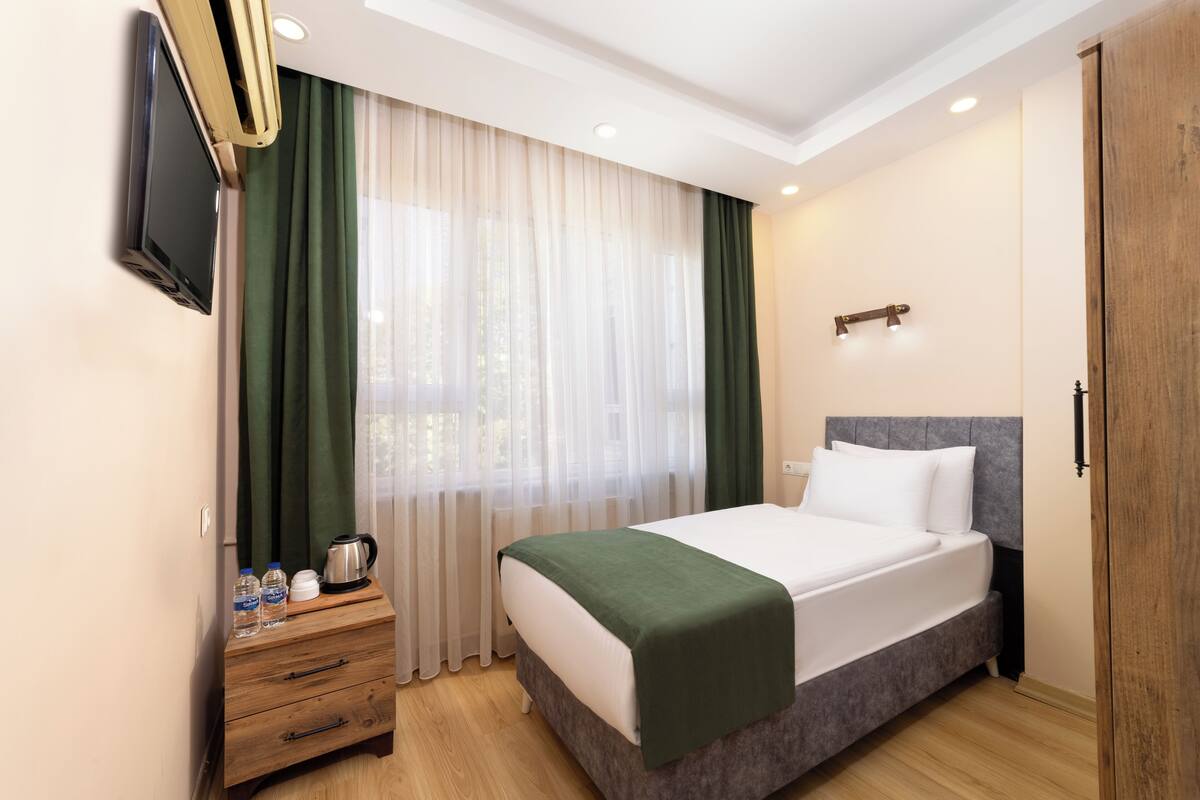 Ein Hotelzimmer mit einem Bett, einem Nachttisch aus Holz mit einem Fernseher, einer Wandleuchte und einem Kleiderschrank.