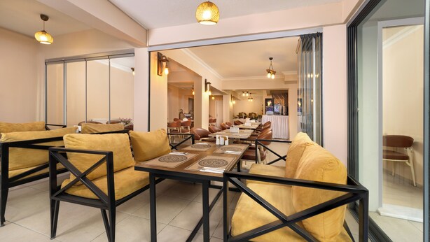 Comedor con mesas y sillas, cocina al fondo y puerta corrediza de vidrio.