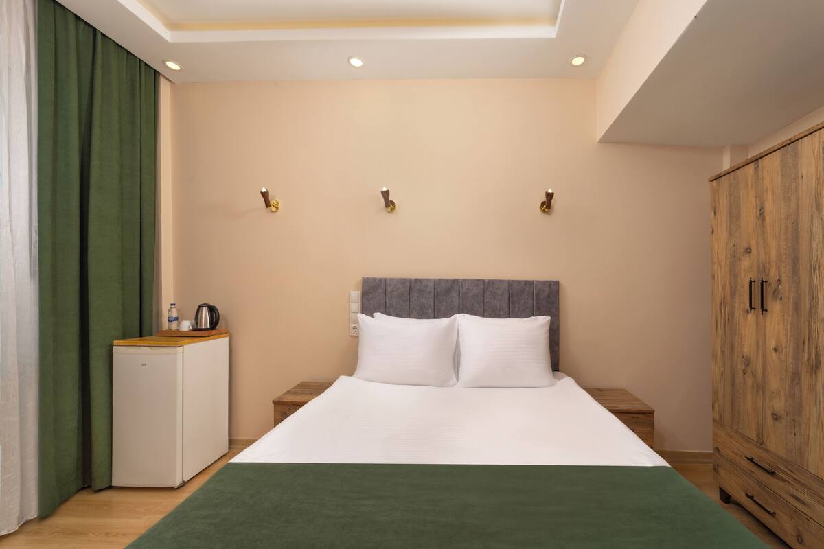 Ein Hotelzimmer mit Bett, Nachttischen, einem Kleiderschrank, einer kleinen Küchenzeile und einem grünen Teppich.