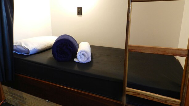 A bunk bed with a black mattress, a rolled-up dark blue blanket, and a white towel. - Utopia Hostel (Aparecida)