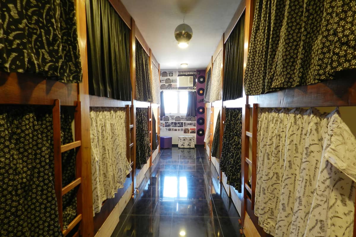 A corridor with patterned curtains on both sides, leading to a room with a disco ball and a display of photographs.