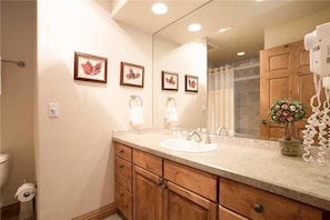 A bathroom with a sink, mirror, wooden cabinets, and framed artwork on the wall.