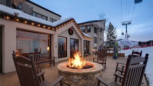 A stone fire pit with chairs, a building with a shop, and a ski lift in the background. - Chateau Chamonix - Cx326 Condominium (Steamboat Springs)