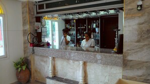 Un mostrador de recepción de mármol con un teléfono, una planta en maceta y un espejo que refleja una zona de bar con estantes llenos de botellas y vasos.