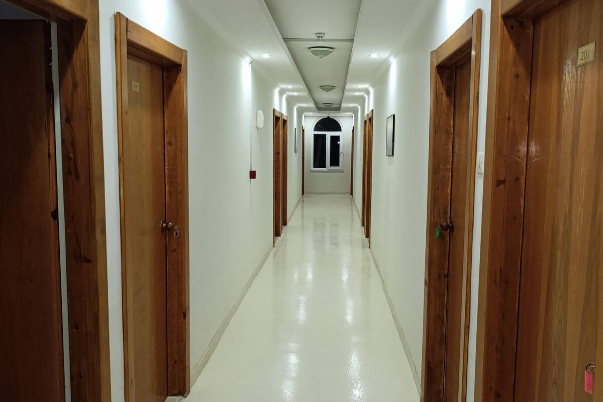 Un largo pasillo bien iluminado con puertas de madera a ambos lados, que conduce a un arco central.