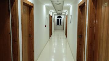 Un long couloir bien éclairé, avec des portes en bois de chaque côté, menant à une porte d’entrée centrale en forme d’arc.