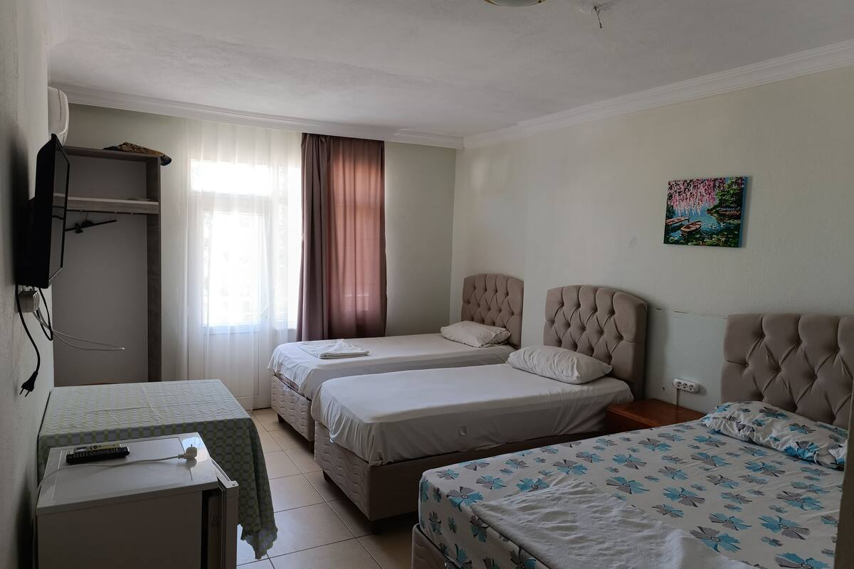 Habitación de hotel con dos camas, un escritorio, televisor y ventana con cortinas.