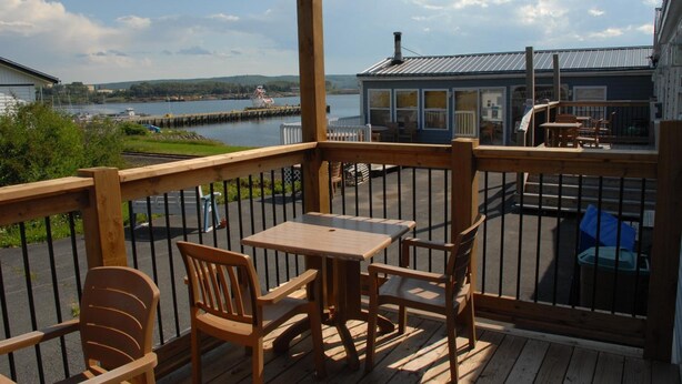 A wooden deck with a table and chairs, overlooking a body of water with boats and a dock. - Harbourview Motel & Accommodations (Port Hawkesbury)