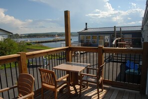 A wooden deck with a table and chairs, overlooking a body of water with boats and a dock.