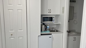 A compact kitchen with white cabinets, a microwave, a small refrigerator, and a sink. - Harbourview Motel & Accommodations (Port Hawkesbury)