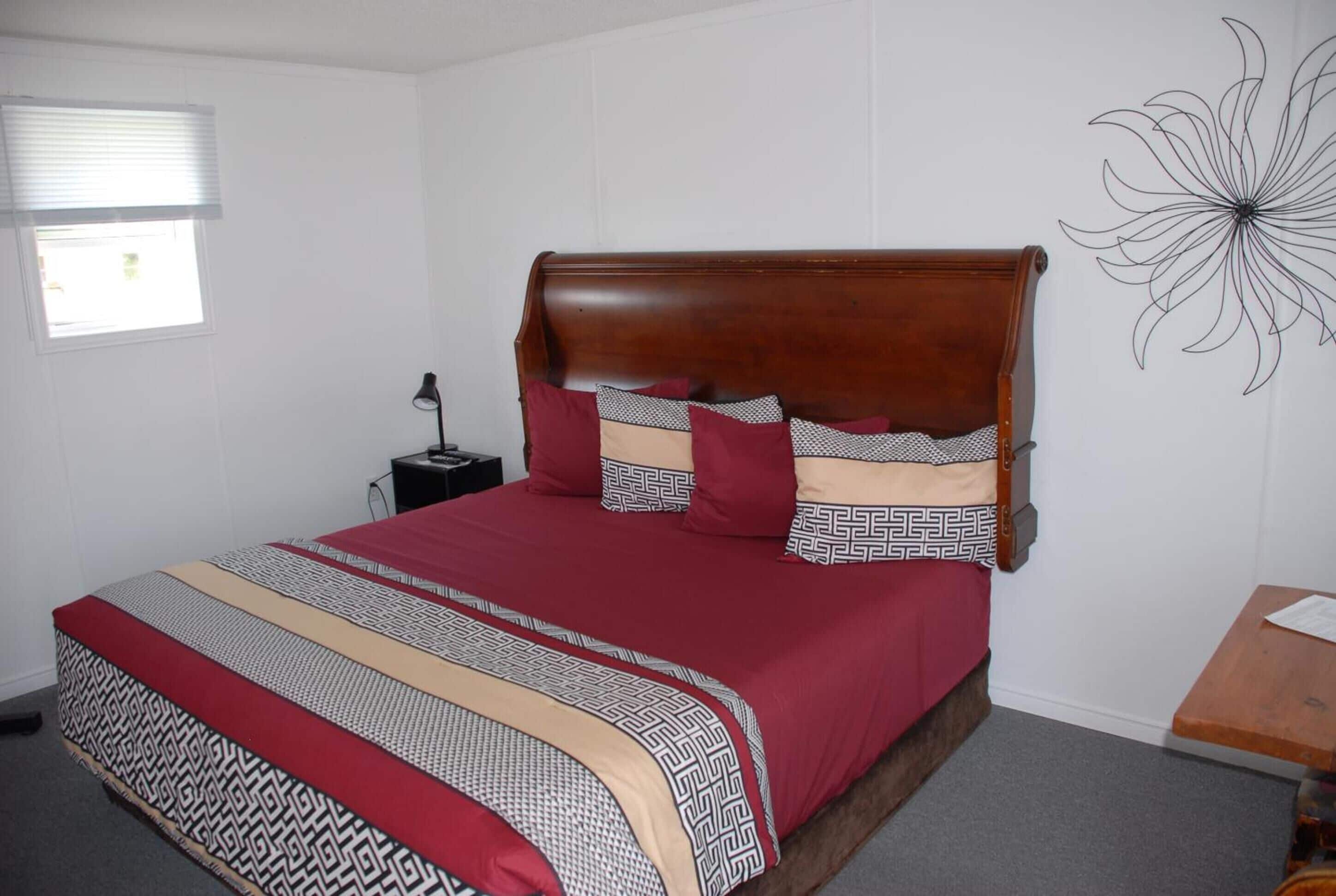 A bedroom with a wooden headboard, a patterned bedspread, and a wall art piece.
