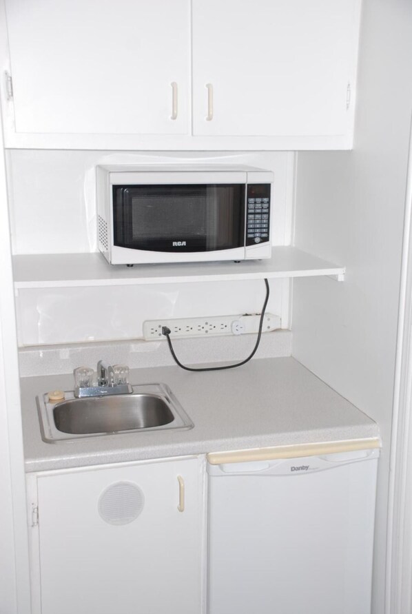 Una kitchenette compacta con un microondas blanco, un lavamanos de acero inoxidable y un lavavajillas Danby.