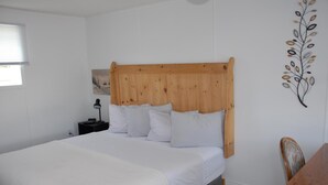 A neatly made bed with a wooden headboard, a bedside table with a lamp, and a wall-mounted artwork. - Harbourview Motel & Accommodations (Port Hawkesbury)