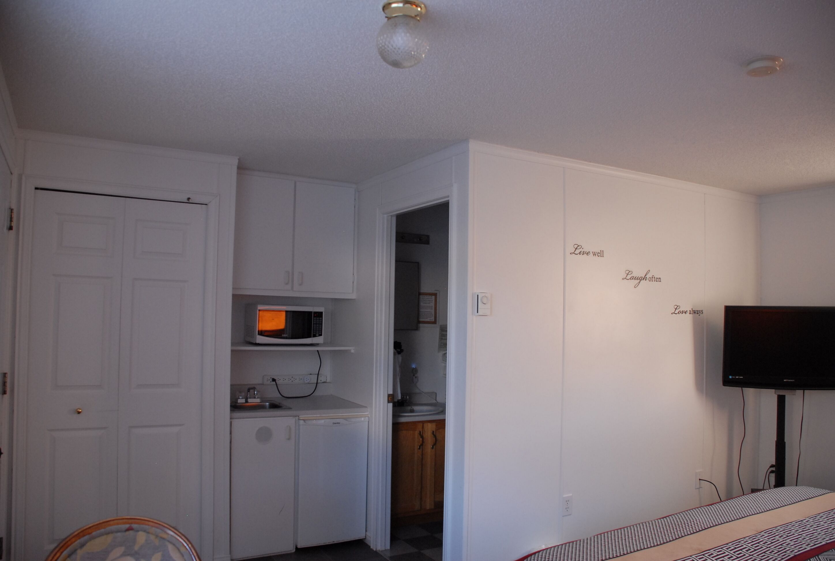 A compact room with a kitchenette, a television, and a door leading to another room.