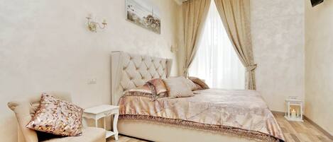 A bedroom with a large bed, a chair, a nightstand, a wall-mounted TV, and a window with curtains.