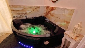 Un jacuzzi negro con un fondo de pared de mármol, una mesita con un objeto decorativo y luces LED a lo largo del borde de la bañera.