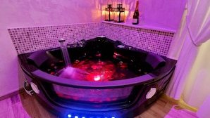 Un jacuzzi con una fuente de agua, rodeado de iluminación morada, y una botella de champán sobre una estantería.