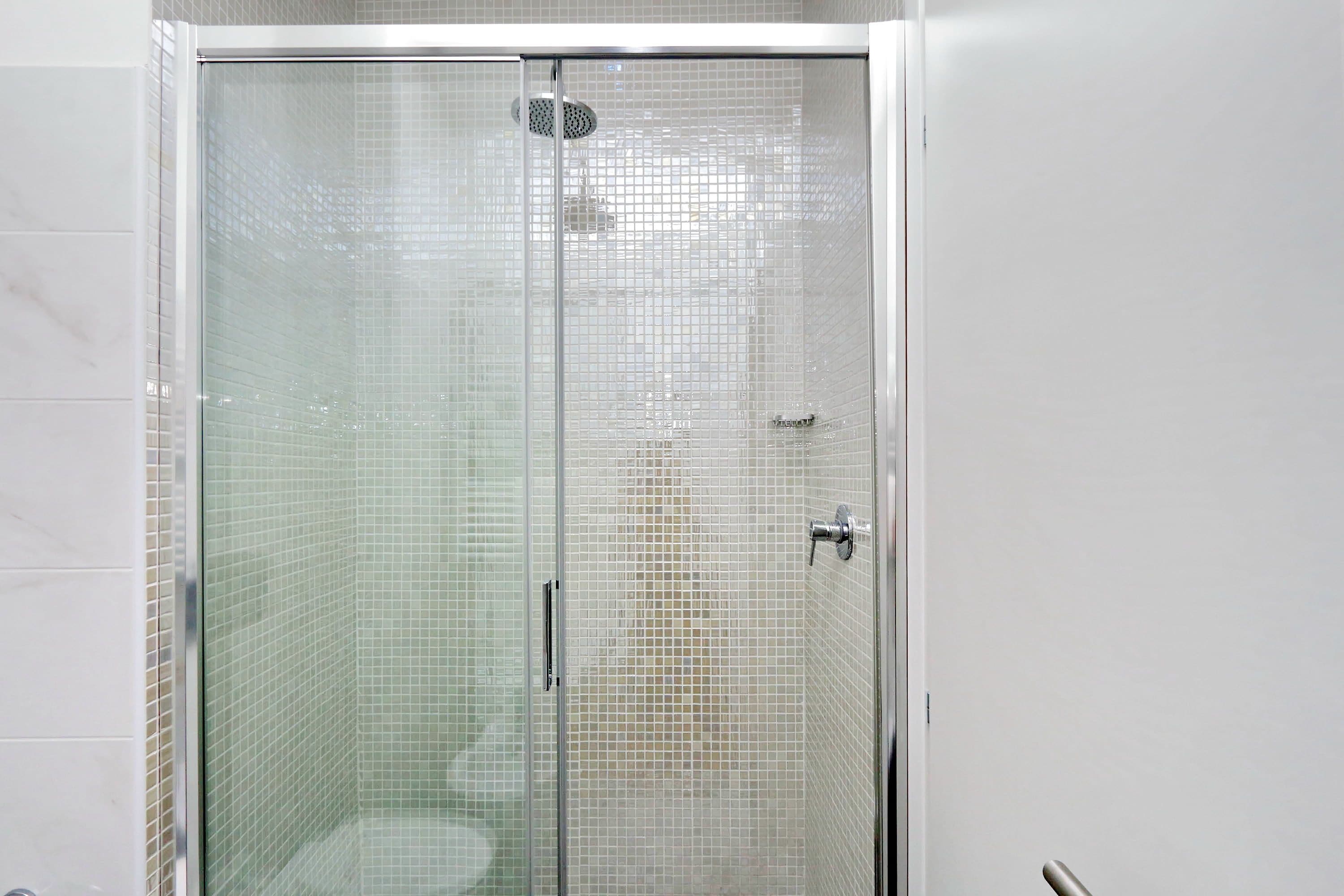 A glass-enclosed shower with a tiled wall and a metallic handle.