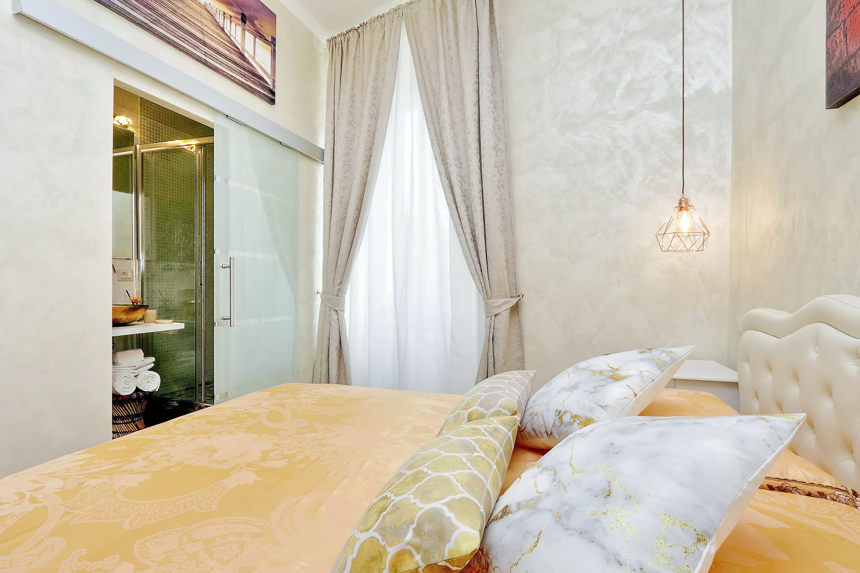 A bedroom with a bed, a hanging light fixture, and a shower area.