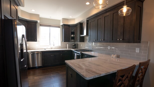 A modern kitchen with dark wood cabinets, stainless steel appliances, a marble island, and pendant lighting. - Just Finished and Furnished!  Spacious Luxury Condo 326 Stimson Ave, Pismo Beach (Pismo Beach)