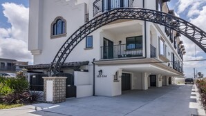 A two-story building with a white facade, a balcony with black railings, and a large arched entrance. - Just Finished and Furnished!  Spacious Luxury Condo 326 Stimson Ave, Pismo Beach (Pismo Beach)
