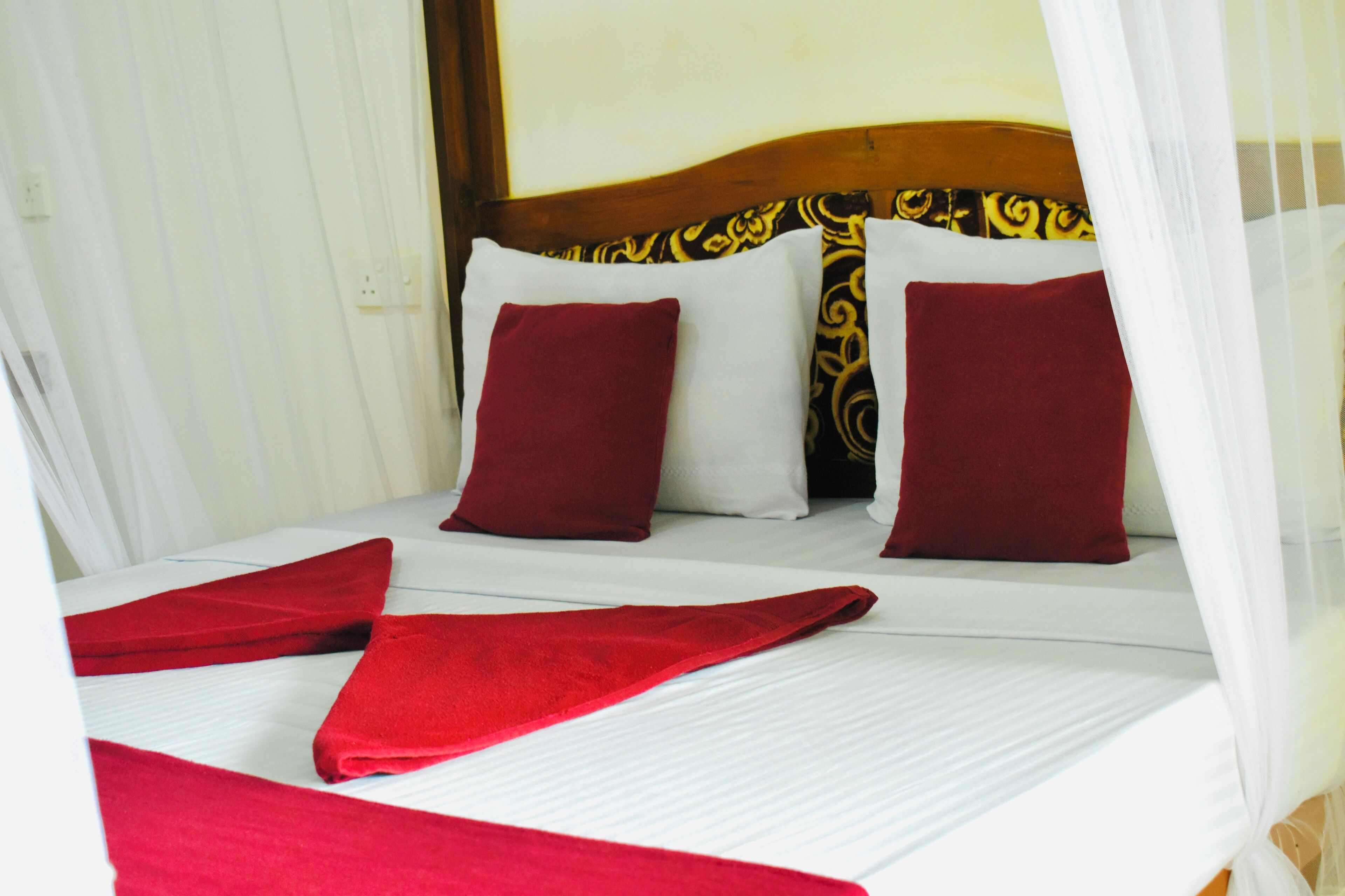 A neatly made bed with white linens and red accents, including pillows and a blanket.