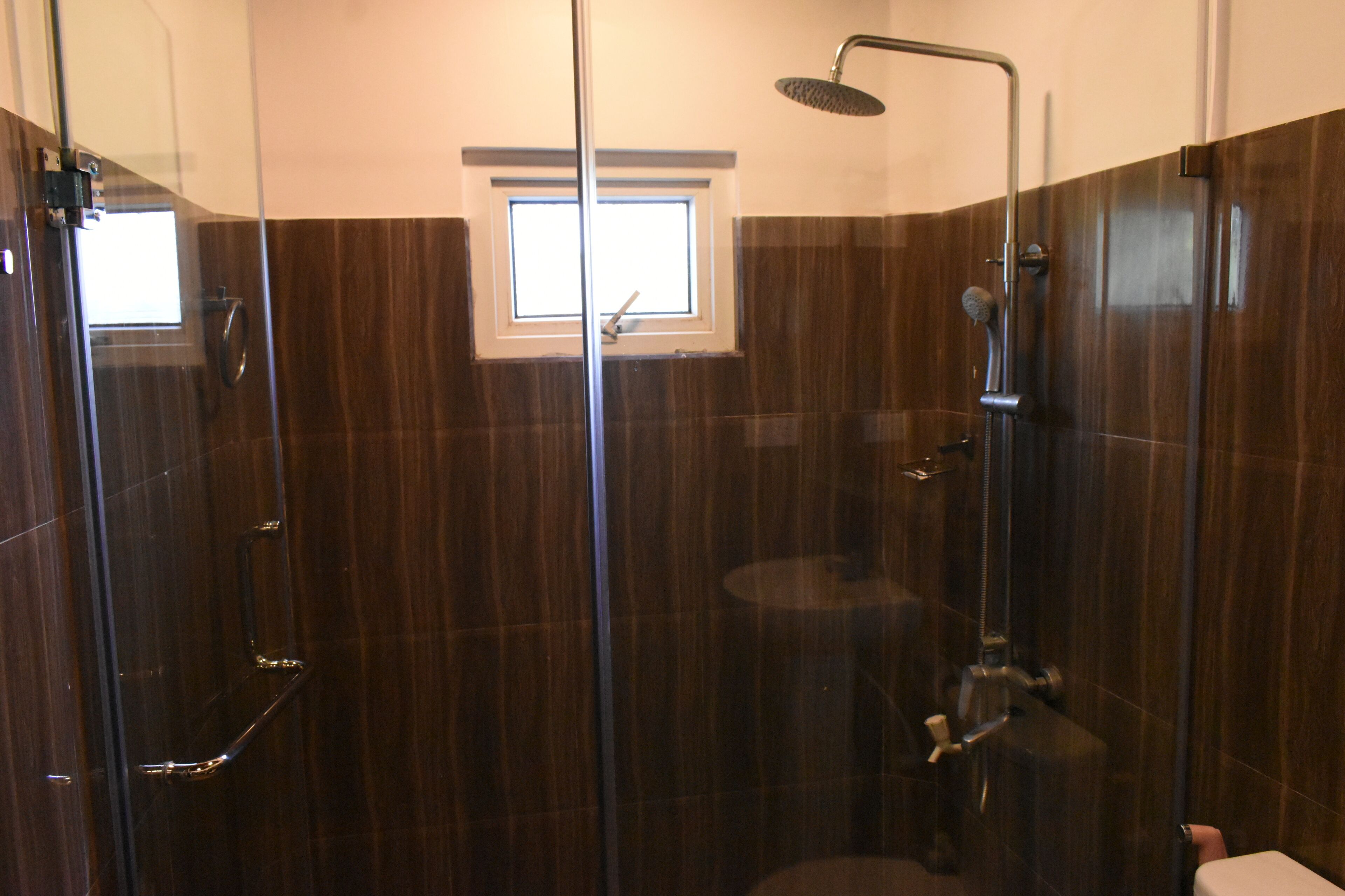 A modern bathroom with a glass-enclosed shower, a small window, and a toilet.