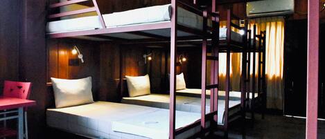 Habitación con literas, un escritorio y una silla, una cama con almohadas, y una ventana con cortinas.