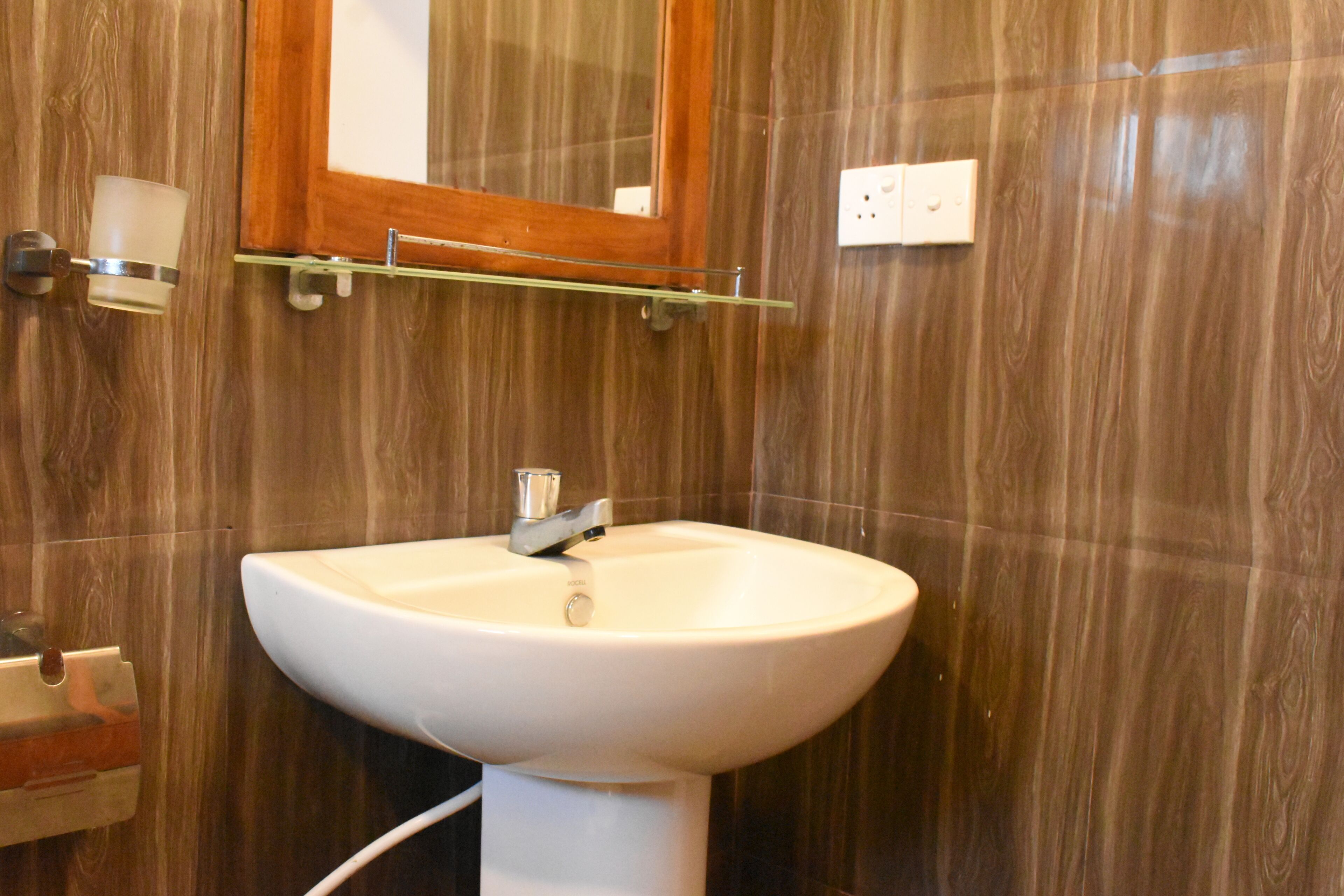 A bathroom with a white sink, wooden wall paneling, a mirror, and a glass shelf above the sink.