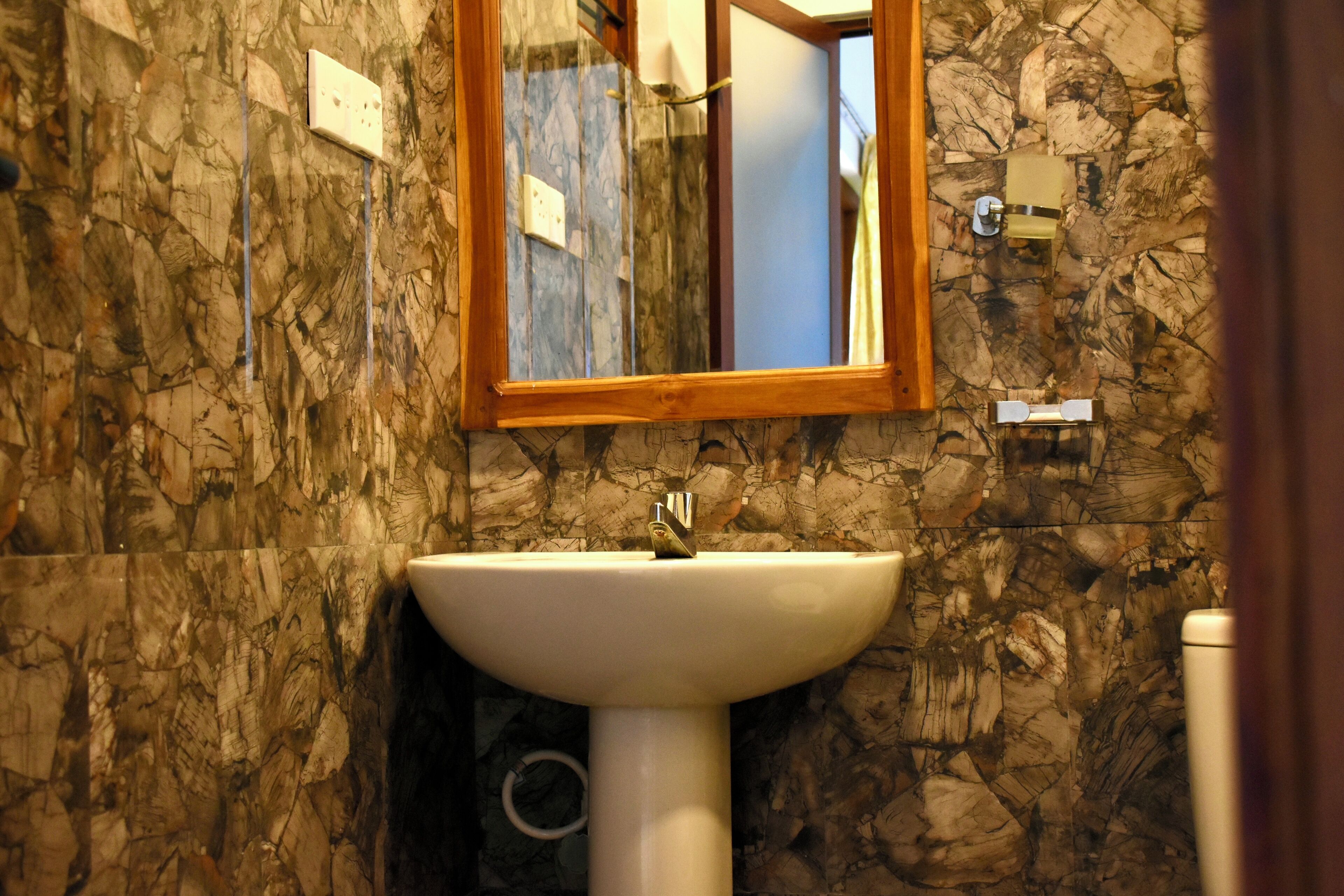 A bathroom with a marble wall, a white sink, and a wooden-framed mirror.