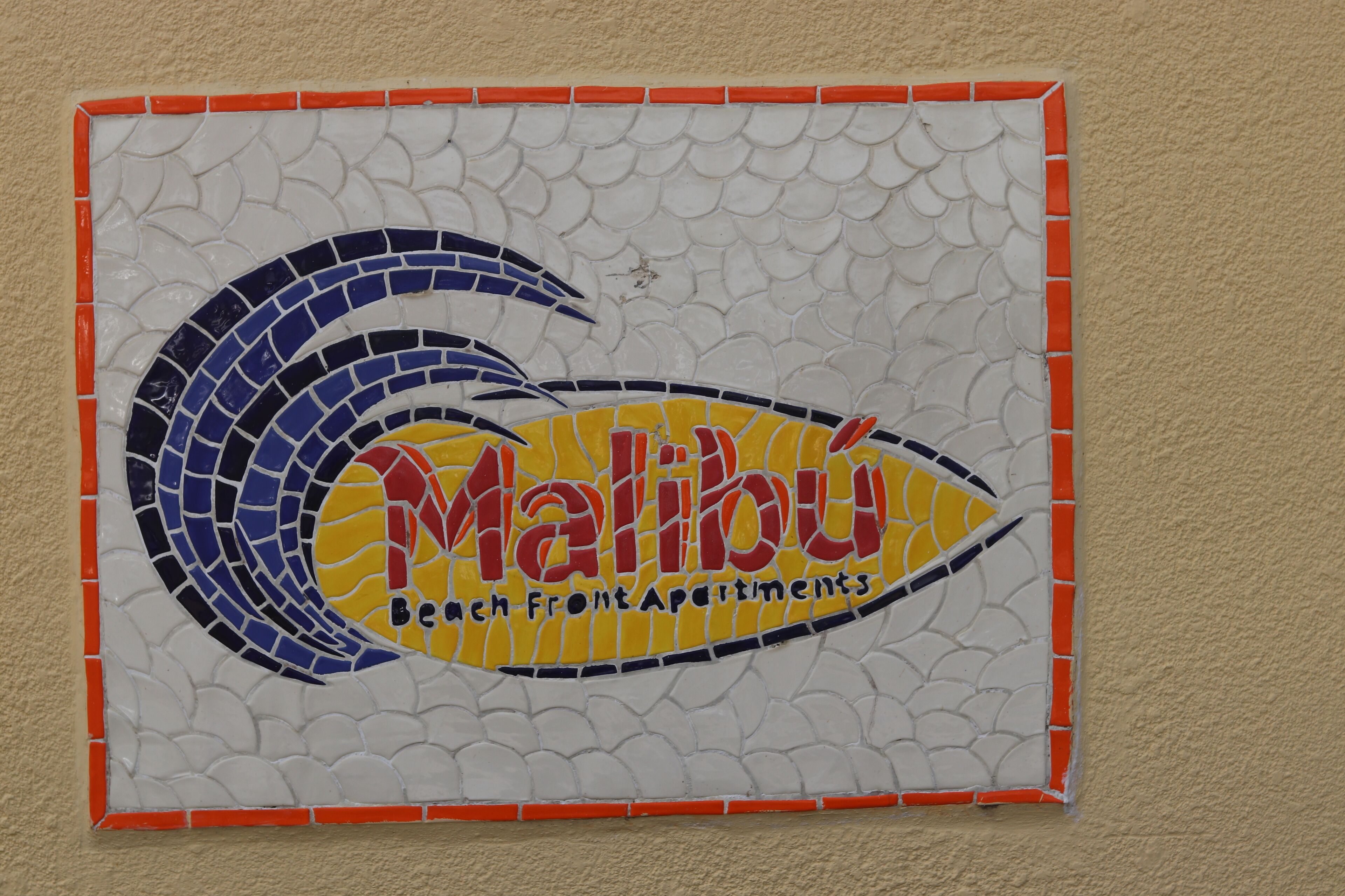A mosaic sign for Malibu Beach Front Apartments with a wave design.