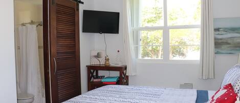 A bedroom with a bed, a TV mounted on the wall, a window with curtains, and a painting on the wall.