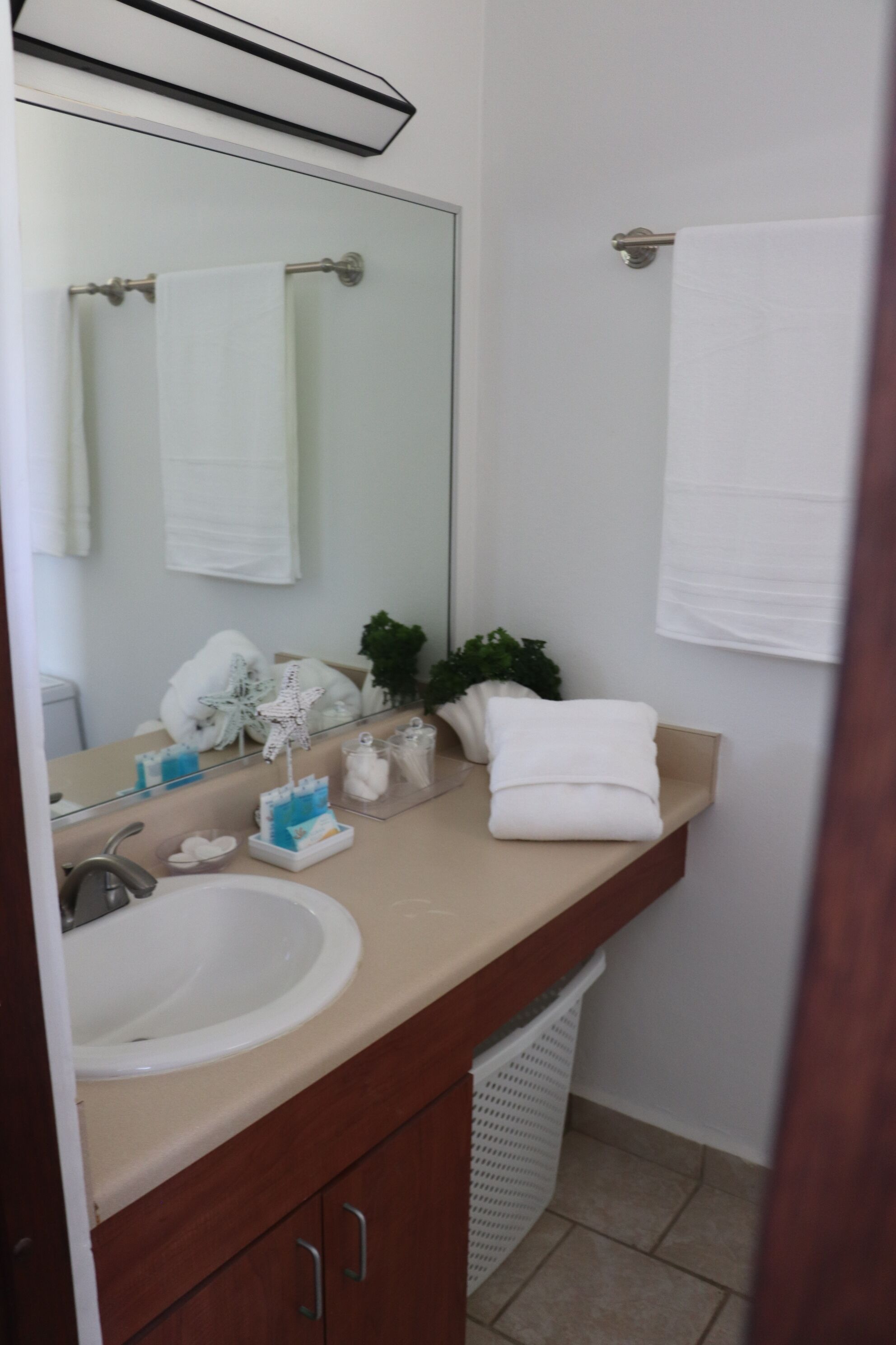 A bathroom with a white sink, a mirror, a towel rack, and a white trash bin.