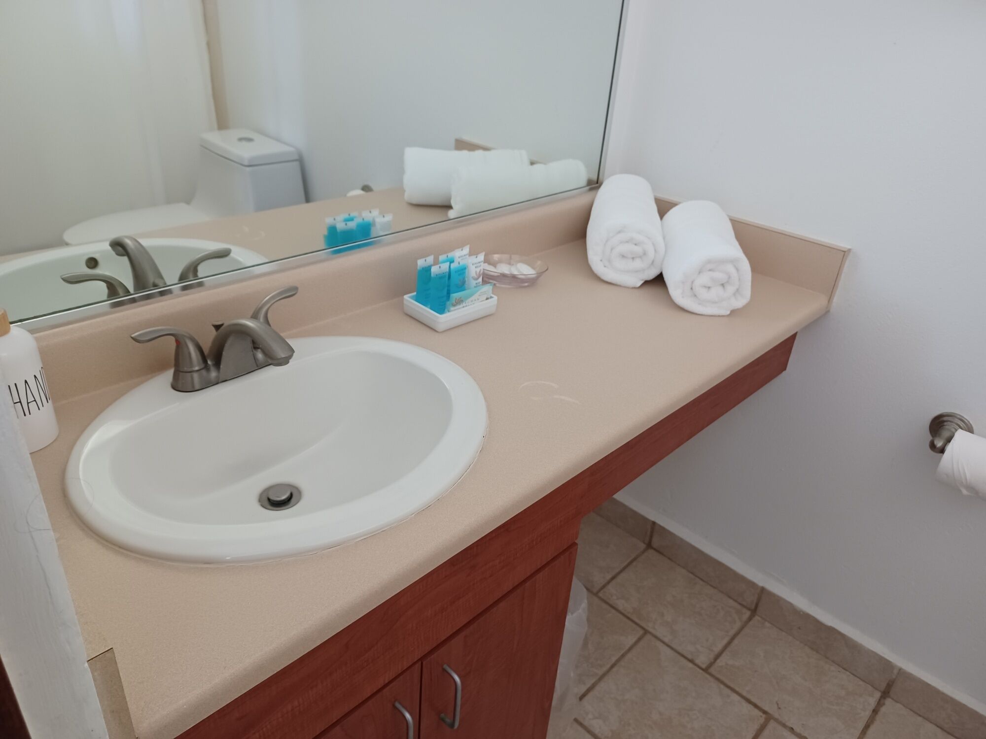Baño con lavamanos, espejo, toallero y artículos de aseo.