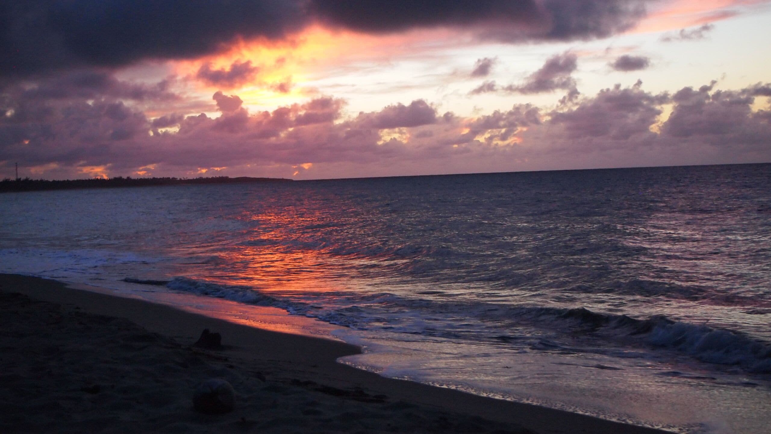 Una playa al atardecer, con olas mansas acariciando la orilla.