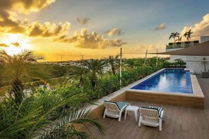 A rooftop pool with two lounge chairs and a view of the sunset.