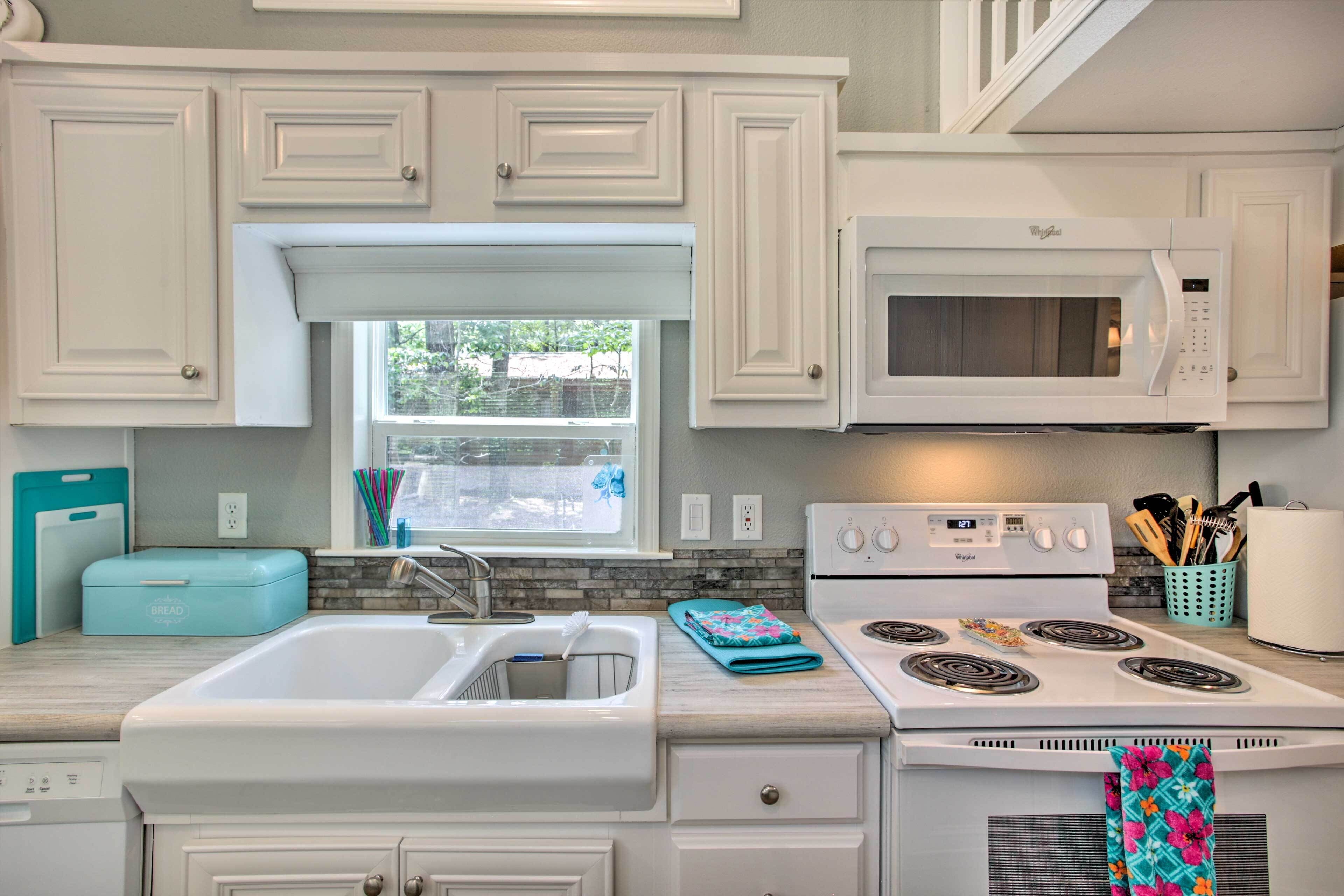 Una cocina con armarios blancos, microondas, estufa y ventana con vistas al exterior.