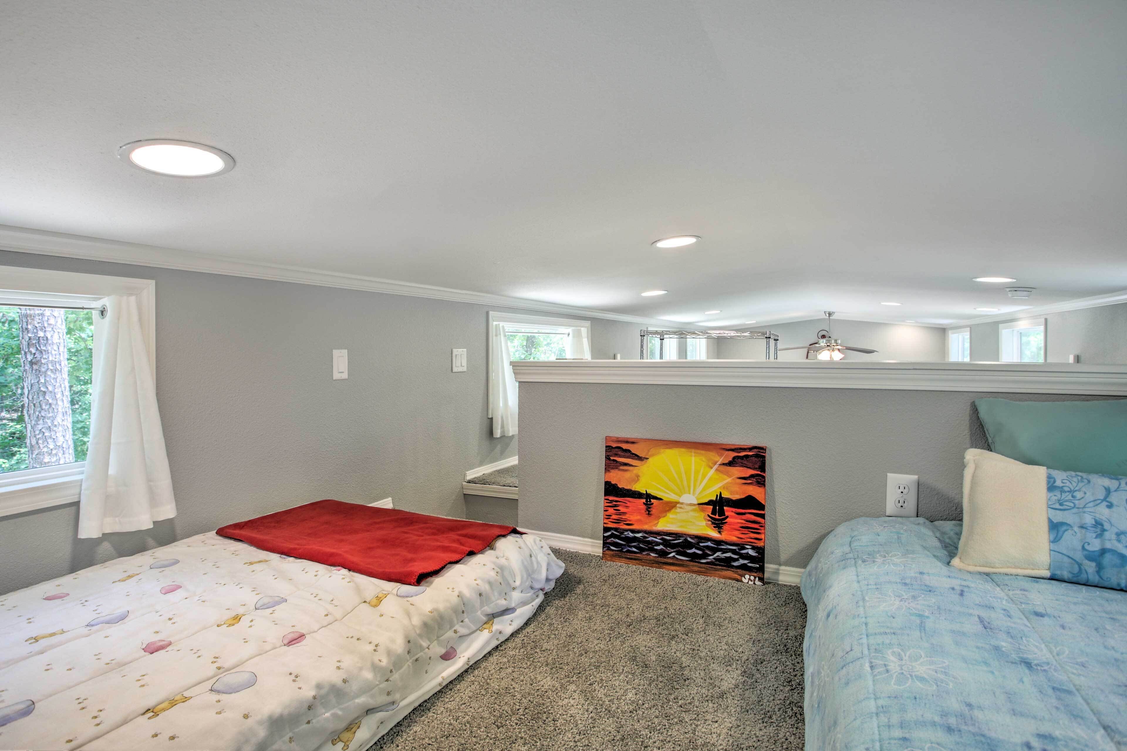 A bedroom with two beds, a ceiling fan, and a painting of a sunset.
