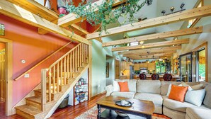 Uma sala de estar ampla com escada de madeira, um amplo conjunto de sofás e uma cozinha ao fundo.