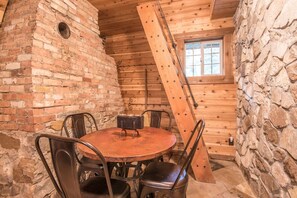 A rustic wooden interior with a brick wall, a round wooden table, metal chairs, and a window with a view of the outside. - Wee Cottage- Unparalleled Charm, Tiny House, Enchanting Setting, Hot Tub (Sundance)