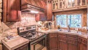 A rustic kitchen with stone walls, wooden cabinets, a stove, and a window with a view of trees. - Wee Cottage- Unparalleled Charm, Tiny House, Enchanting Setting, Hot Tub (Sundance)