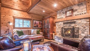 A cozy cabin interior with a stone fireplace, wooden walls, a sofa, leather chairs, and a table with a book. - Wee Cottage- Unparalleled Charm, Tiny House, Enchanting Setting, Hot Tub (Sundance)